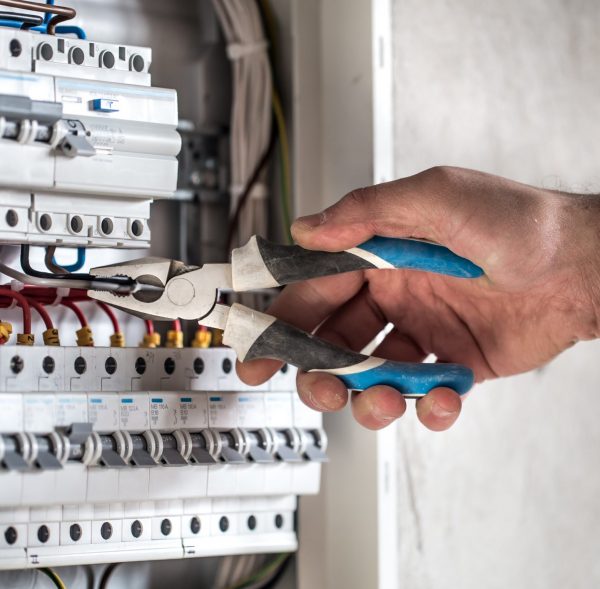 Man, an electrical technician working in a switchboard with fuses. Installation and connection of electrical equipment. Professional with tools in hand. concept of complex work, space for text.